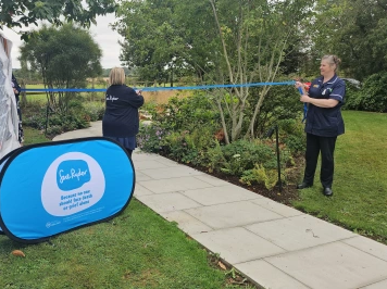 Jacqui, dressed in dark blue Sue Ryder nurse's uniform, cuts a blue ribbon across the new garden's path.