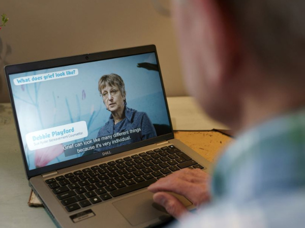 View over the shoulder of a man watching one of Sue Ryder's Grief Kind classes on a laptop
