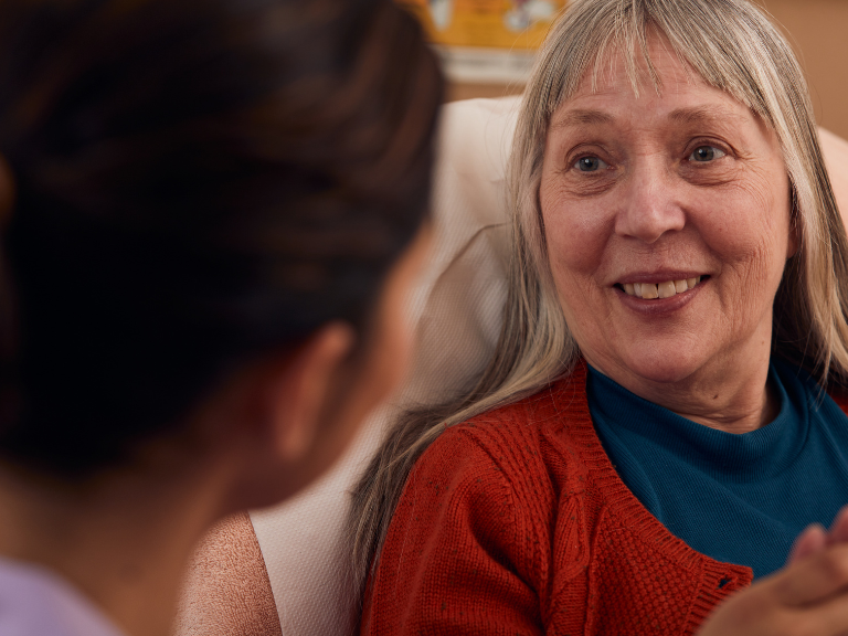 Patient sat up in her bed, smiling at a member of the Sue Ryder care team
