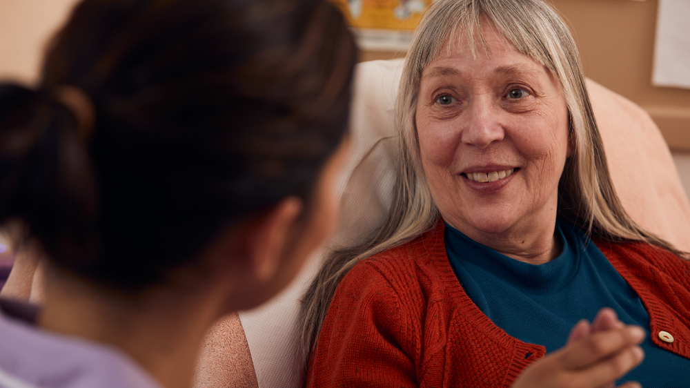 Patient sat up in her bed, smiling at a member of the Sue Ryder care team
