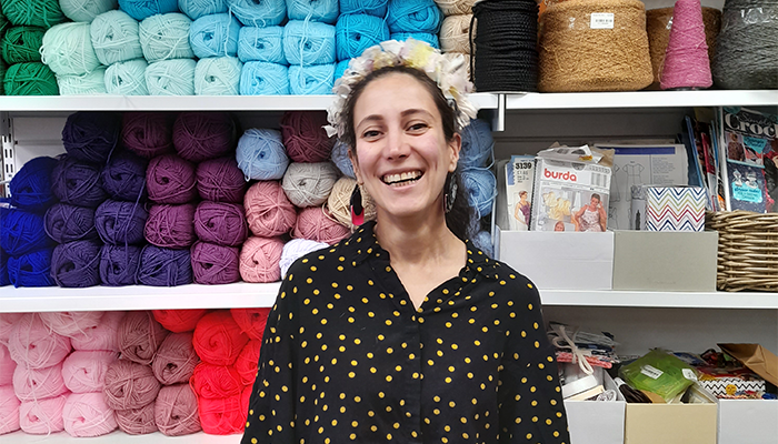 Sue Ryder volunteer Aida stands smiling in front a brightly coloured shop display of wool