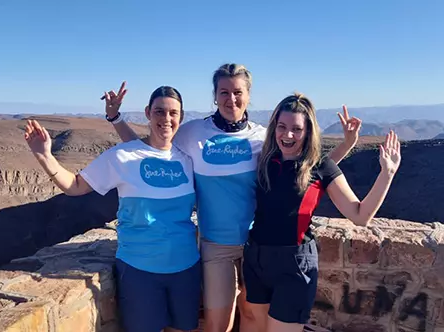 3 people stand in front of mountain view smiling and posing for the camera