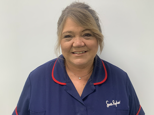 Bobby smiles, wearing her dark blue Sue Ryder nurses uniform.
