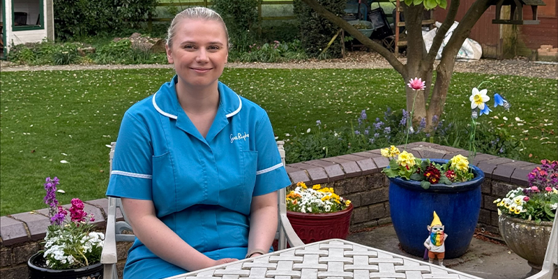Ellen sits at a white table in a colourful flowering garden.