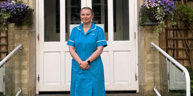 Ellen stands, dressed in her Sue Ryder uniform, in front of white double doors at Sue Ryder St John's Hopsice.