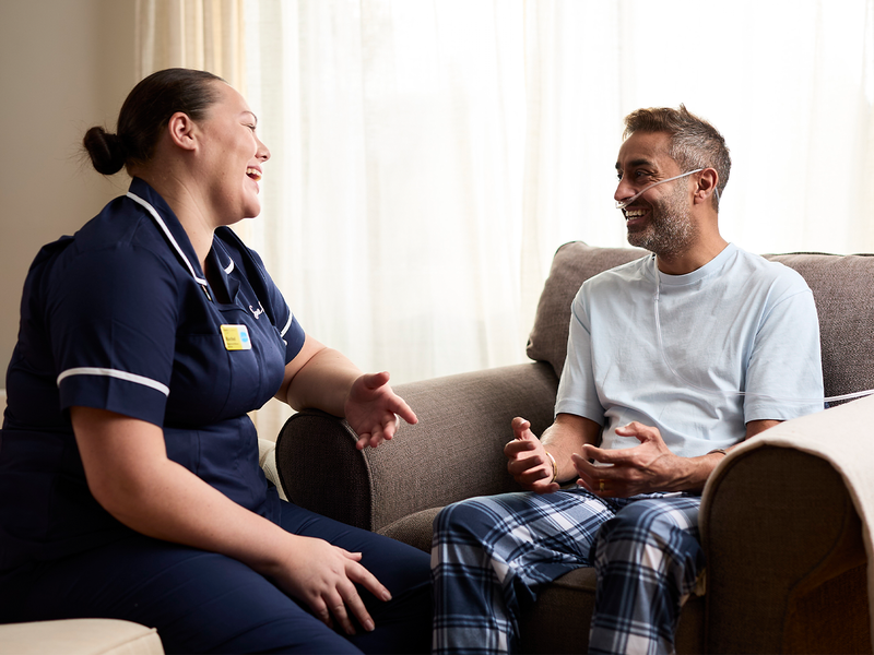 Sue Ryder nurse and patient sit together in a cosy homely room laughing together