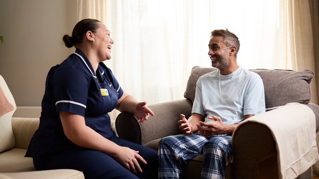 Sue Ryder nurse and patient sit together in a cosy homely room laughing together