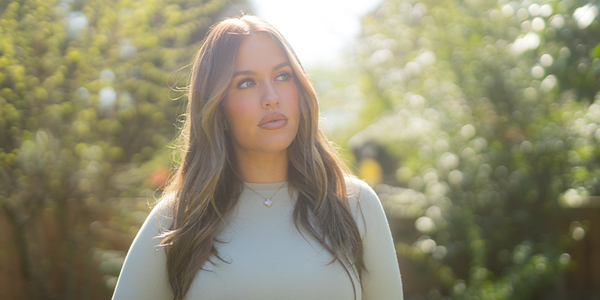 Lottie Tomlinson looks thoughtfully to the side, soft focused green trees in the background