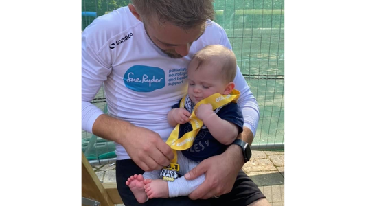 Baby Mark sits on Luke's lap, wearing Leeds Half Marathon medal