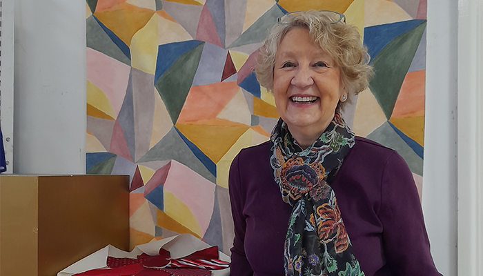 Shop volunteer Mavis stands in front of a painting