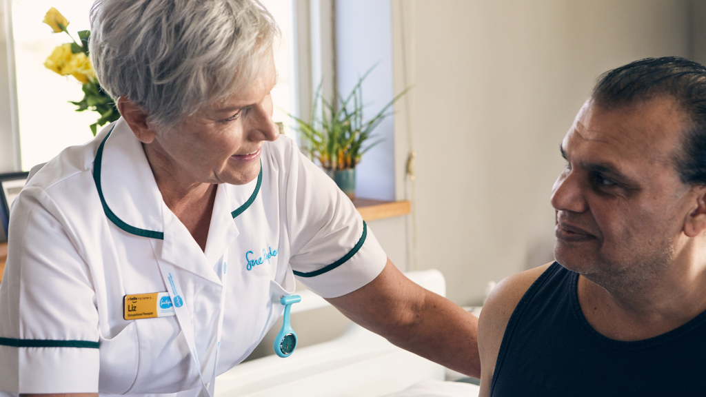 Occupational therapist in white uniform cares for man lying in bed