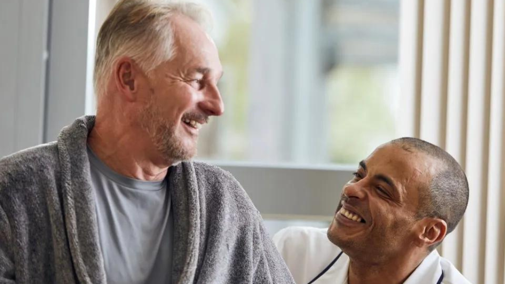 Man in dressing gown looks down at nurse crouching beside him