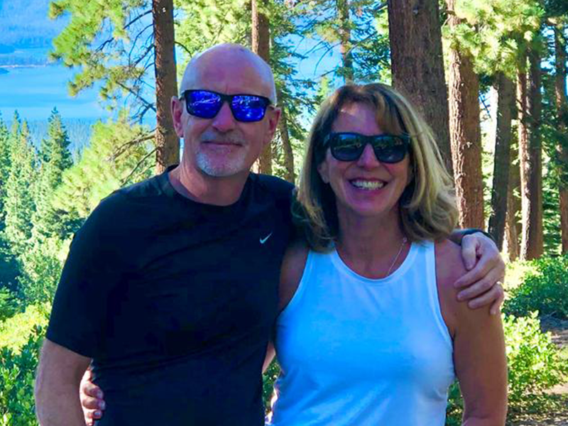 Phil and Anna stand in a rich green forest with water in background