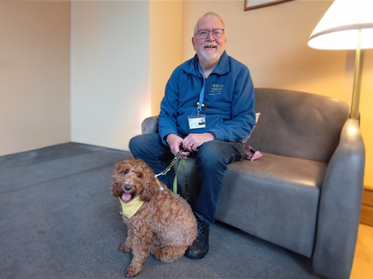 Richard sits holding Jack the cockapoo's lead