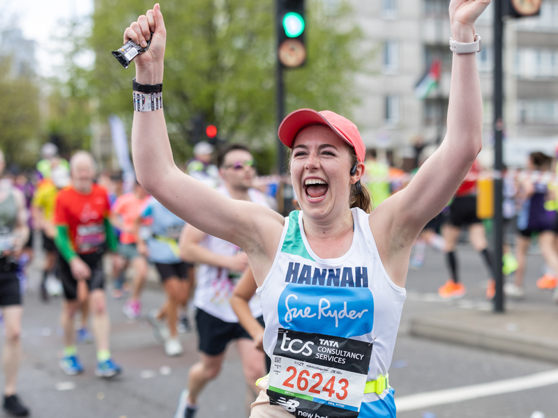Sue Ryder runner smiling running past cheerpoint, with arms in the air in celebration