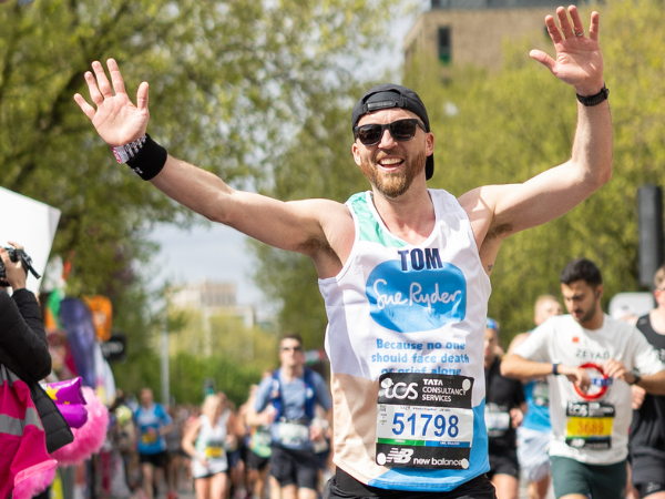 Male Sue Ryder runner waving arms in the air running past cheer point