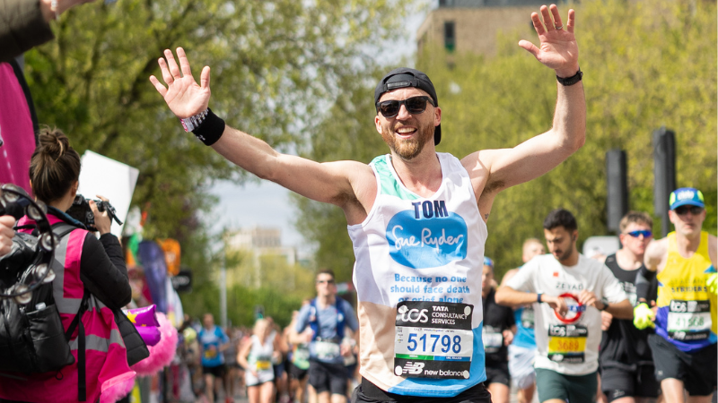 Male Sue Ryder runner waving arms in the air running past cheer point