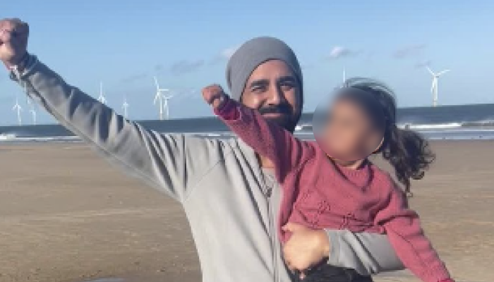 Blurry image of Tony holding one of his children, looking joyful, on a beach. Their hands are in the air.