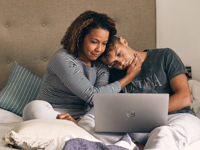 Woman comforts teenager on bed while looking at laptop