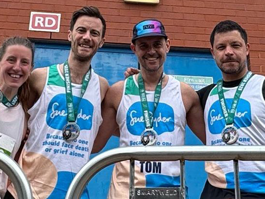 Three brothers in Sue Ryder running vests and a friend pose in front of a stadium