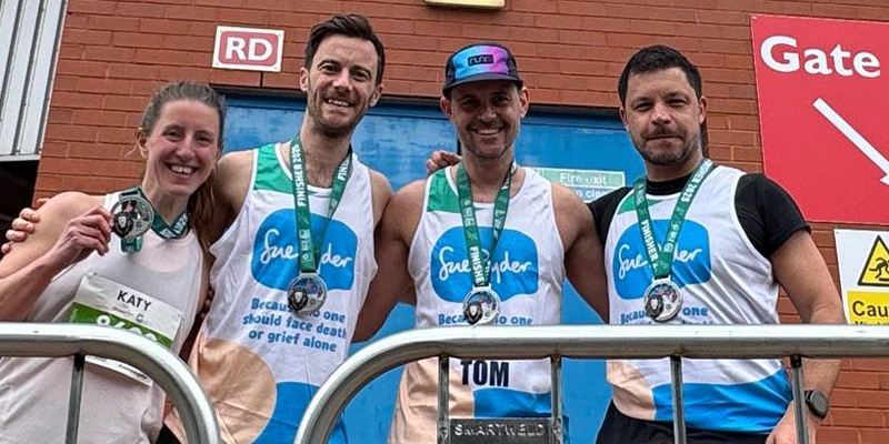 Three brothers in Sue Ryder running vests and a friend pose in front of a stadium